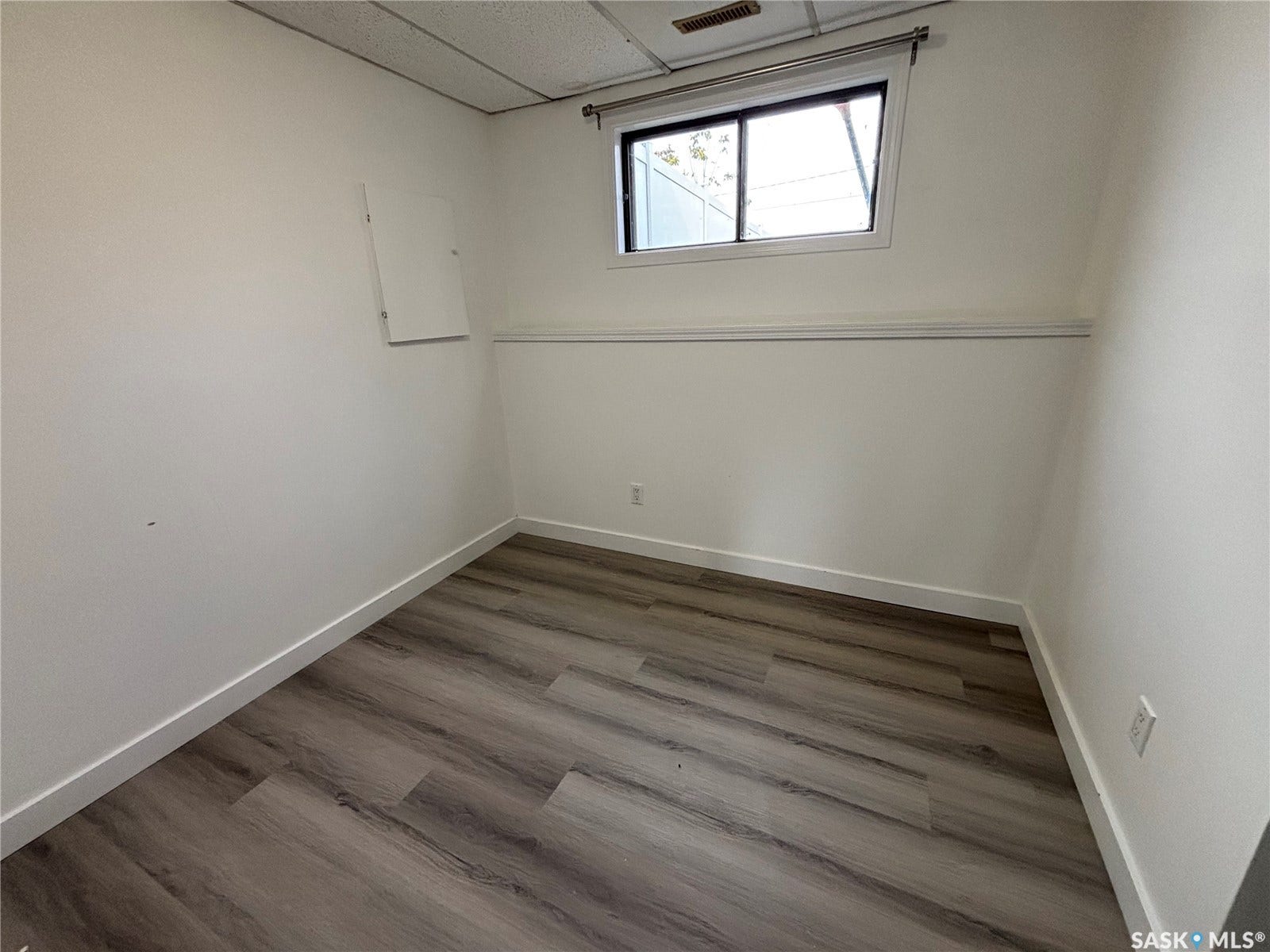Wood-finish flooring, drop ceiling, white walls, and a single window