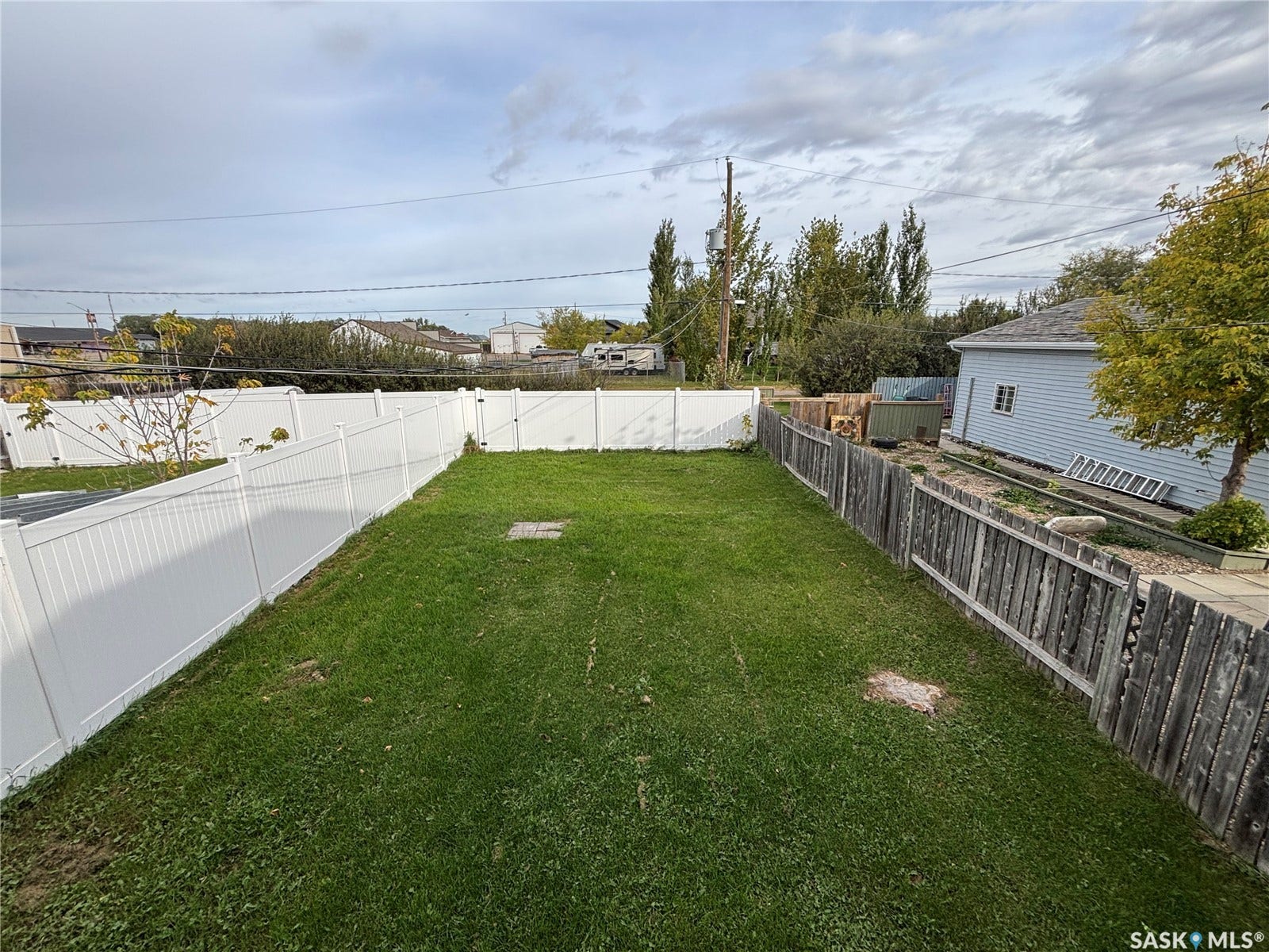 Expansive green lawn with a white privacy fence and partial wood fence