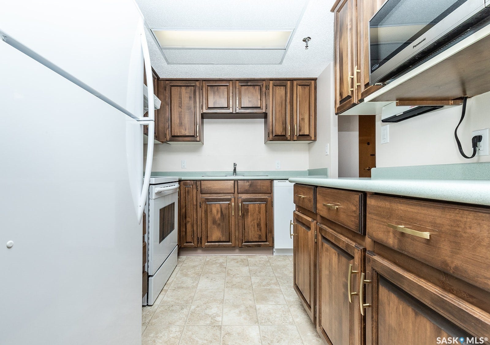 Kitchen featuring wood cabinetry, light-toned countertops, a double basin sink, white appliances and linoleum flooring