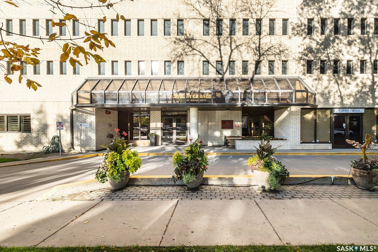 Multi-level building featuring a brick facade, covered glass entrance, and mature landscaping
