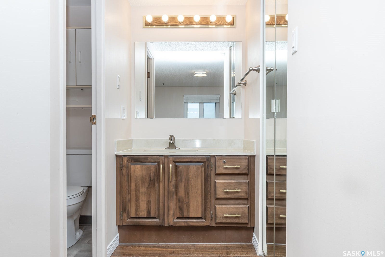 2-piece ensuite bathroom featuring a wood-finish vanity with a light-toned countertop, an overhead vanity light fixture, and a wall-mounted mirror
