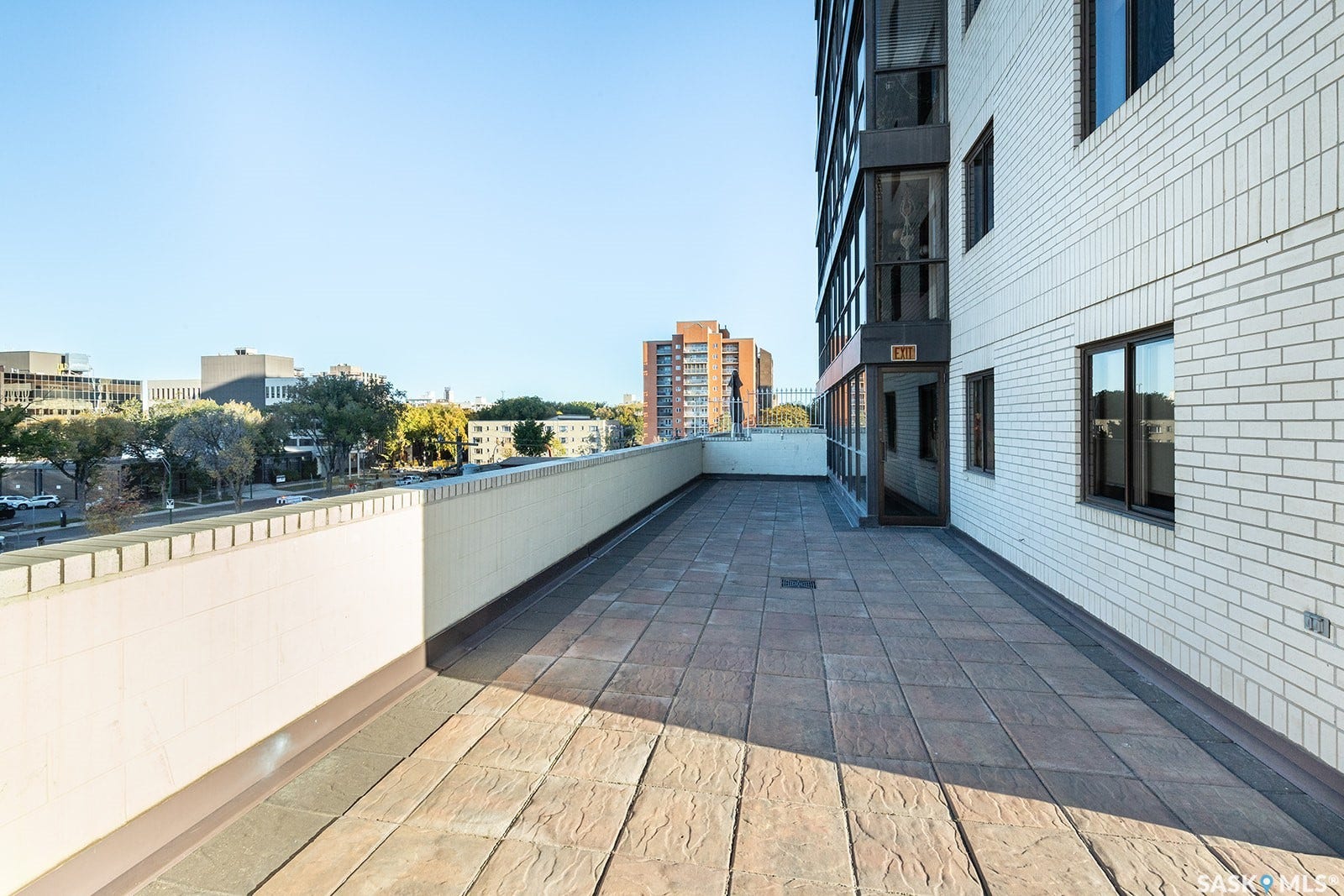 Expansive outdoor terrace featuring textured paver flooring, a white brick exterior, and dark-framed windows