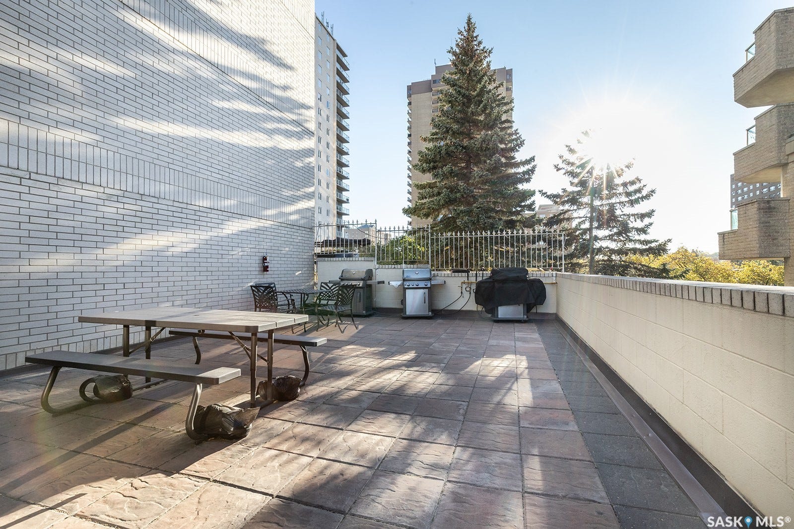 Expansive outdoor terrace with picnic area, barbecues and featuring textured stone tile flooring, a white brick exterior wall, and a low cream-colored perimeter wall