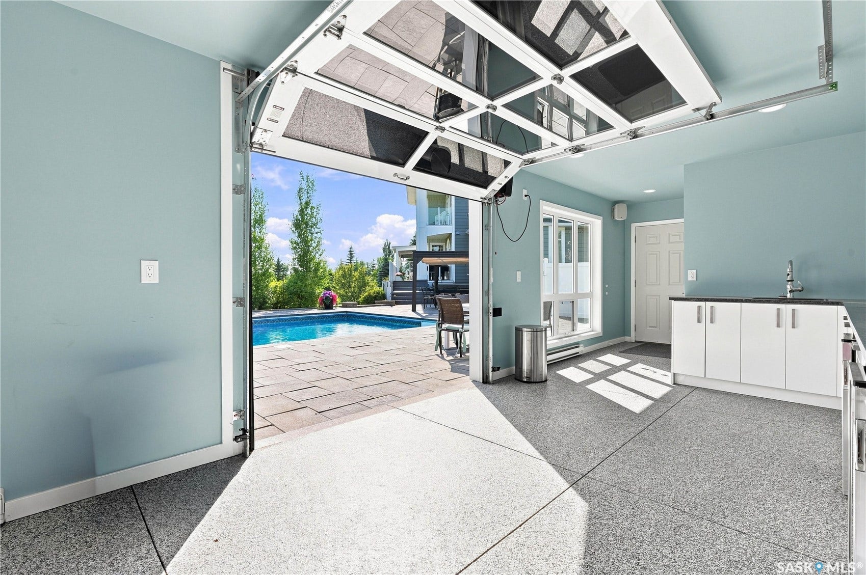 Garage featuring an overhead glass door, epoxy flooring, built-in cabinetry with a sink, and an exterior patio with a pool
