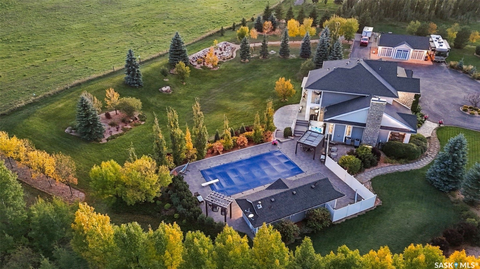 Expansive property featuring a covered swimming pool, stone patio, attached two-story residence with a prominent chimney, a separate outbuilding, and a paved driveway