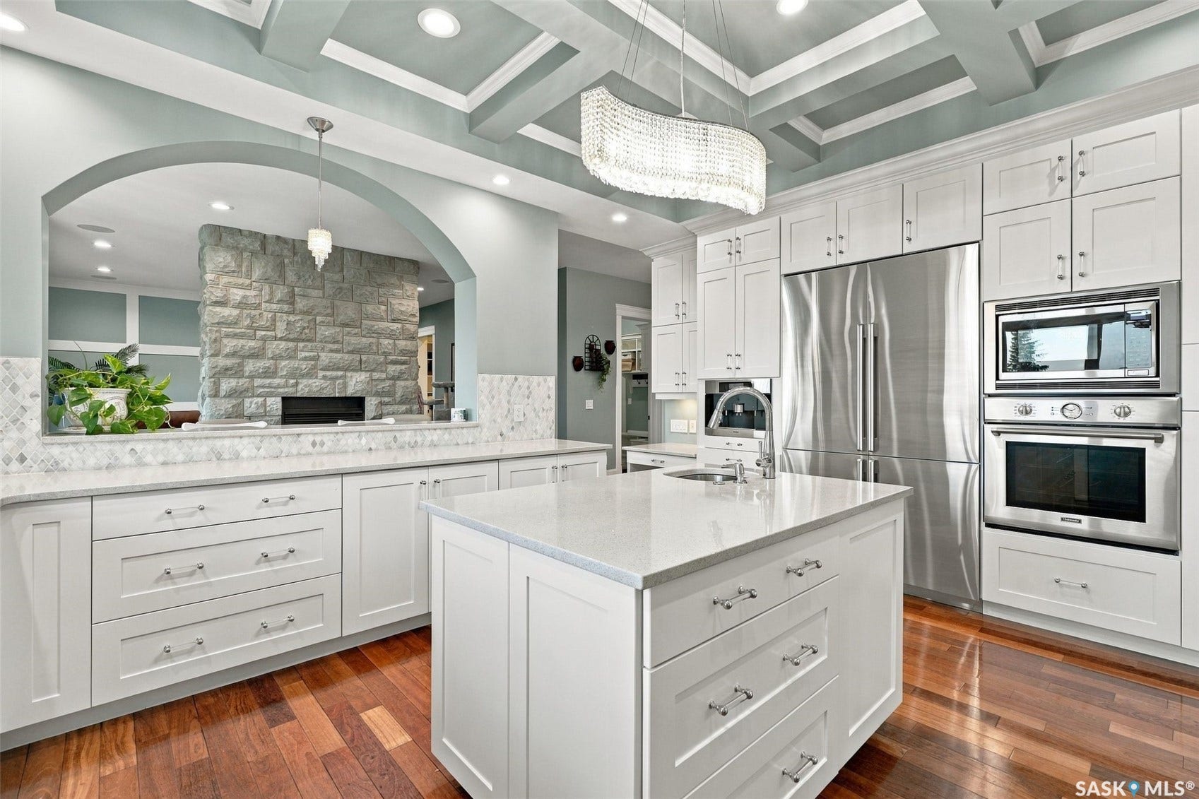 White shaker cabinetry with stone countertops, stainless steel appliances, a multi-level coffered ceiling, and wood-finish flooring