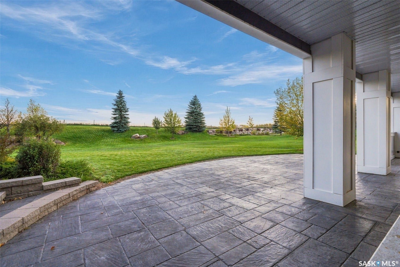 Spacious outdoor patio with stamped concrete flooring, white architectural columns, and a terraced retaining wall leading to a manicured lawn