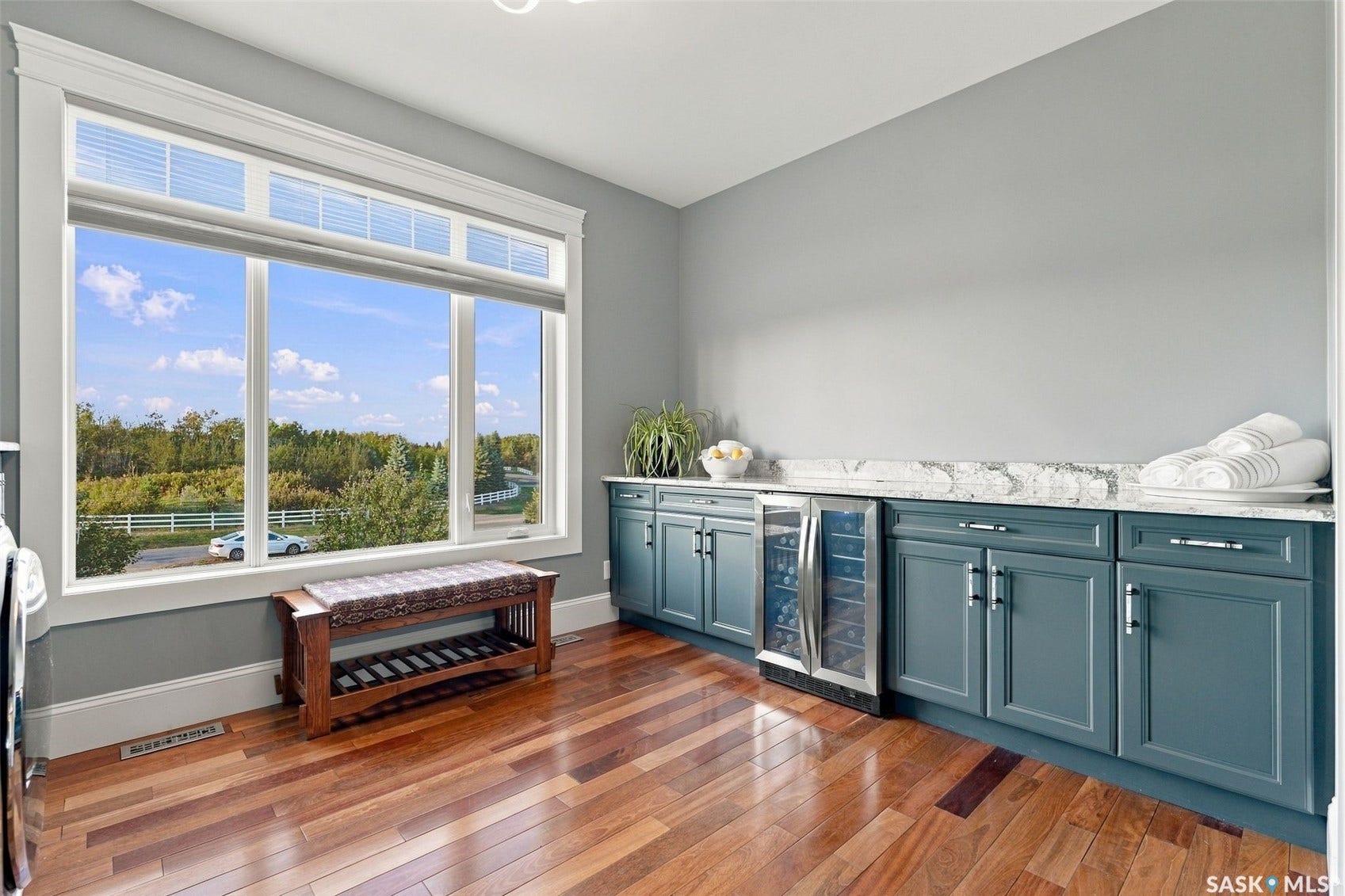 Wide plank wood-finish flooring, built-in cabinetry with a beverage cooler, solid surface countertops, and a large window with transom feature
