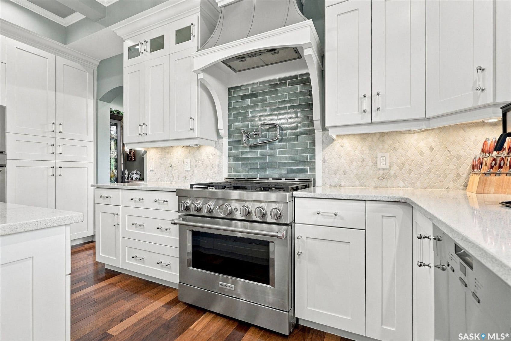Gourmet kitchen featuring stainless steel range, white shaker cabinetry, quartz countertops, wood-finish flooring, and subway tile backsplash