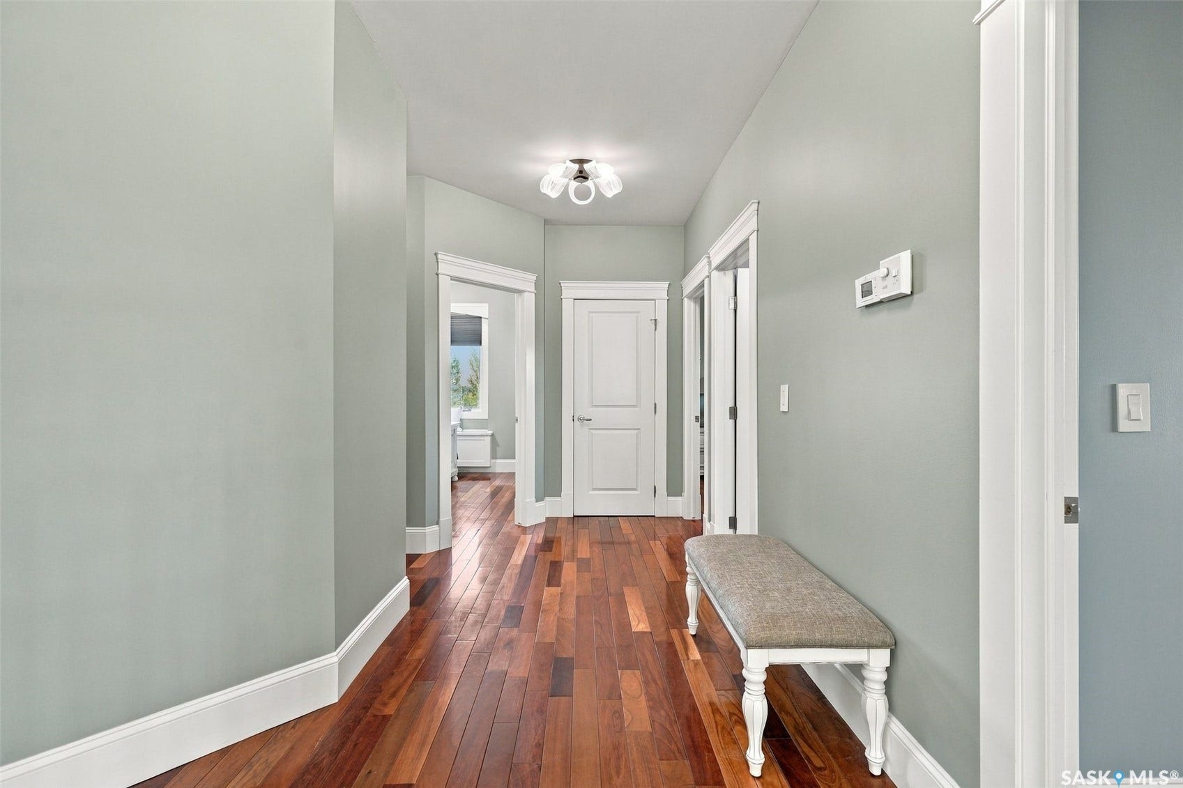 Hardwood flooring extending through the hallway, white trim, and a contemporary flush-mount ceiling light fixture