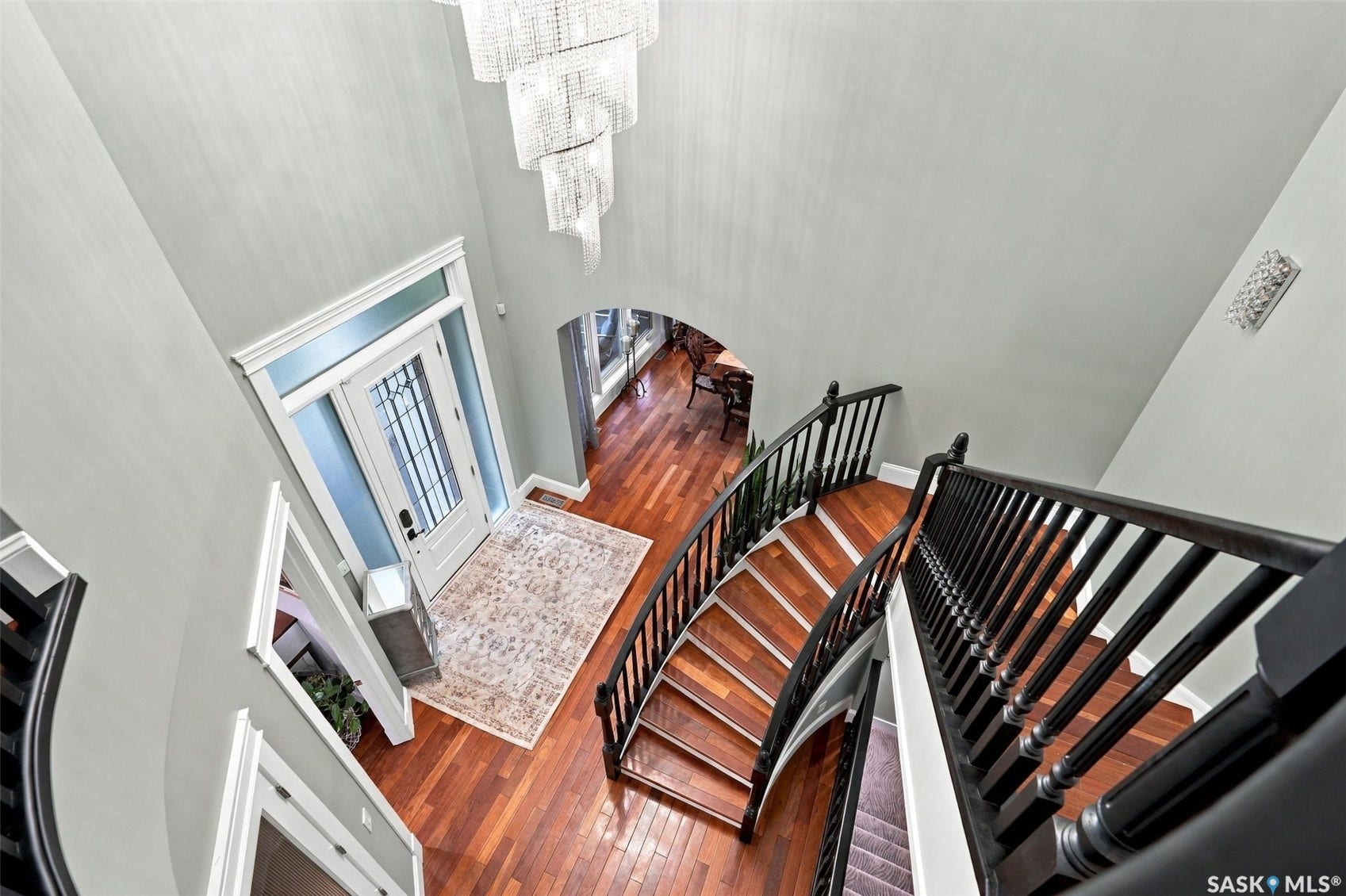 Two-story foyer featuring a grand staircase with dark wood-finish railings, warm-toned wood-finish flooring, an arched entryway, and a prominent multi-tiered chandelier