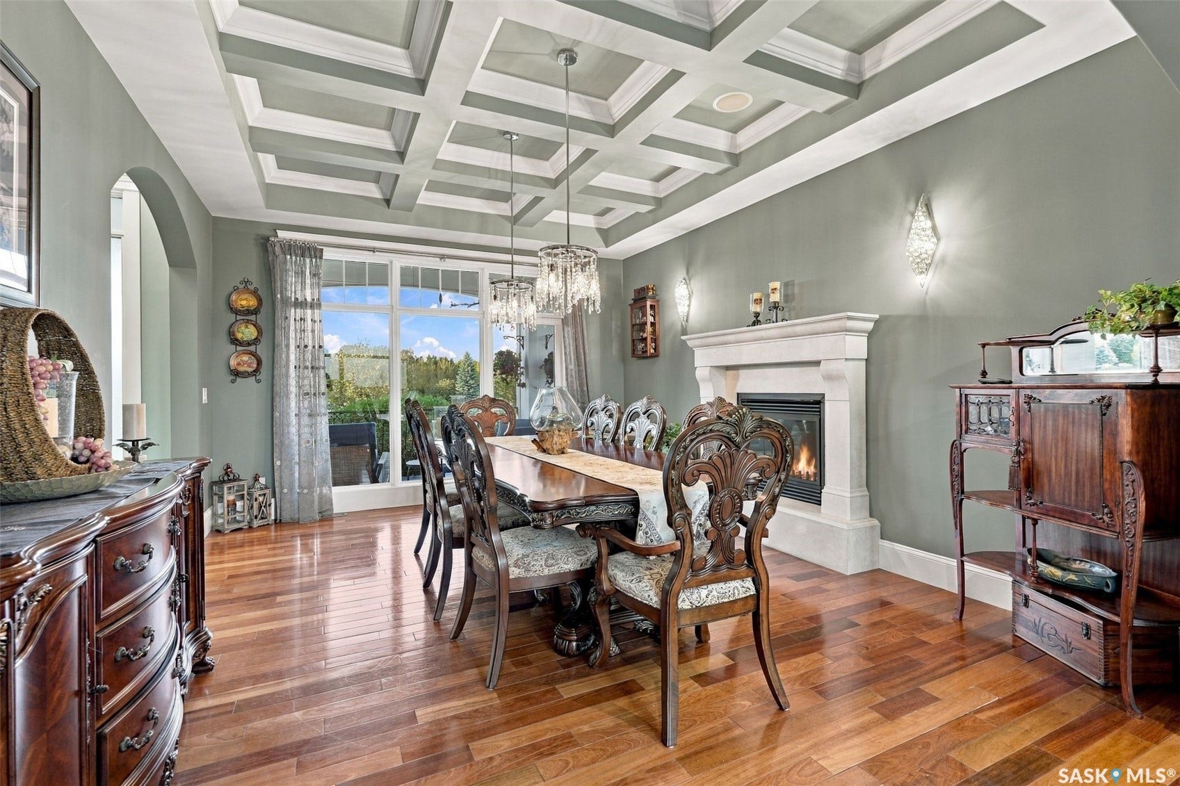 Coffered ceiling design, wood-finish flooring, stone-surround fireplace, arched doorway, and large glass paneled doors