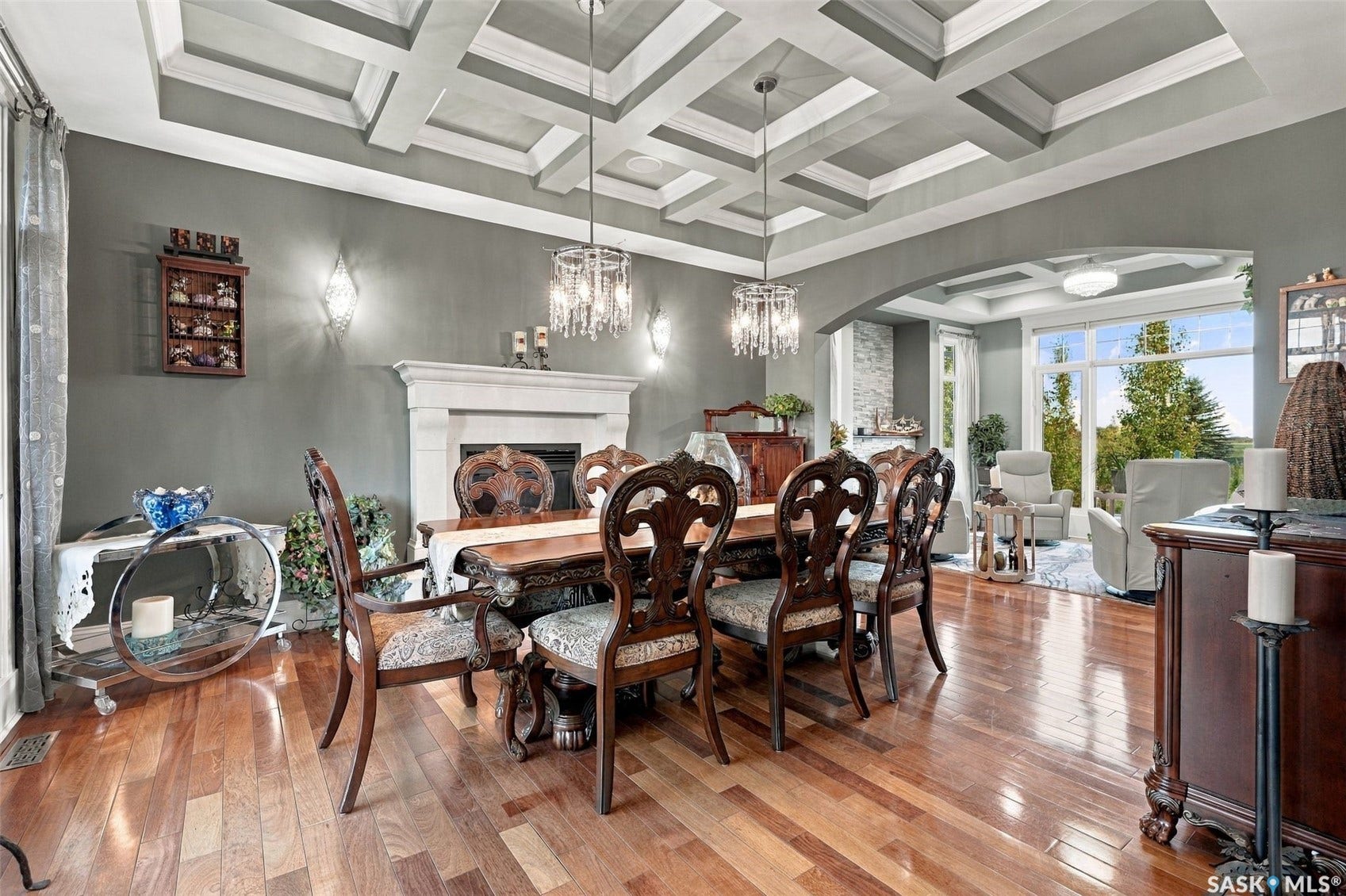 Coffered ceiling with dual chandeliers, fireplace with mantel, hardwood flooring, and arched entryway