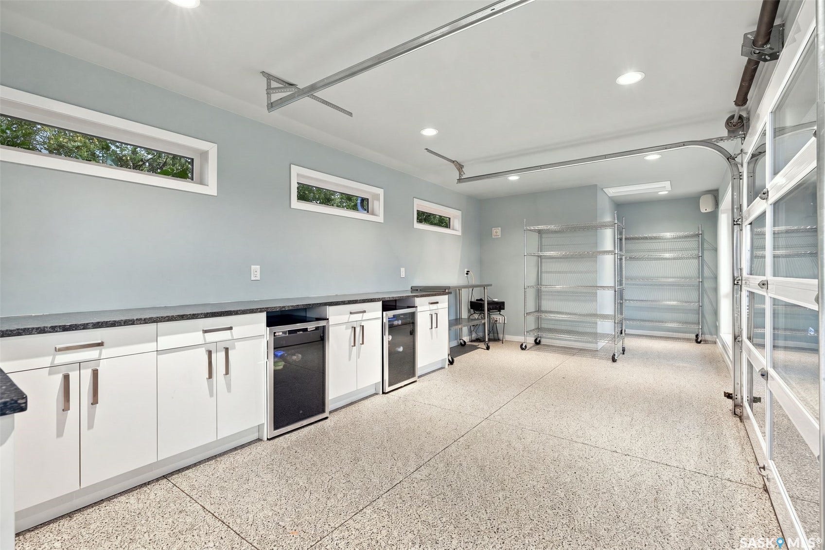 Epoxy flooring, white cabinetry, integrated under-counter appliances, recessed lighting, and a glass-paneled garage door