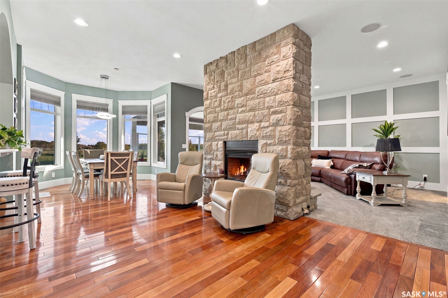 Stone fireplace feature, wood-finish flooring, recessed lighting, bay window, and wainscoting