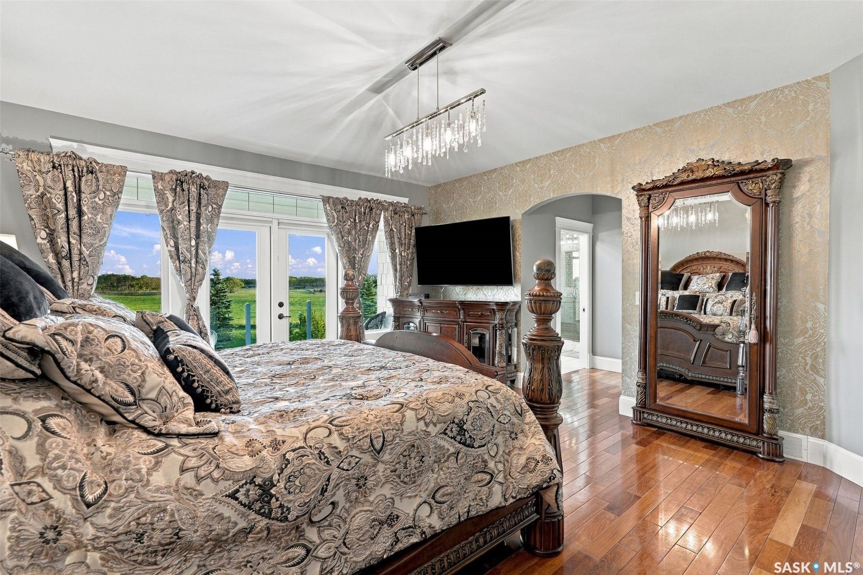 Hardwood flooring, French doors, textured accent wall, arched doorway, and a contemporary linear chandelier