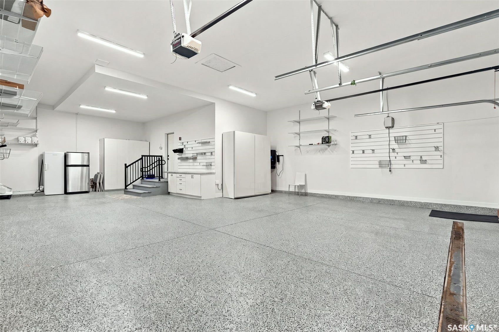 Spacious garage with epoxy flooring, white walls, built-in cabinetry, and modular wall storage systems
