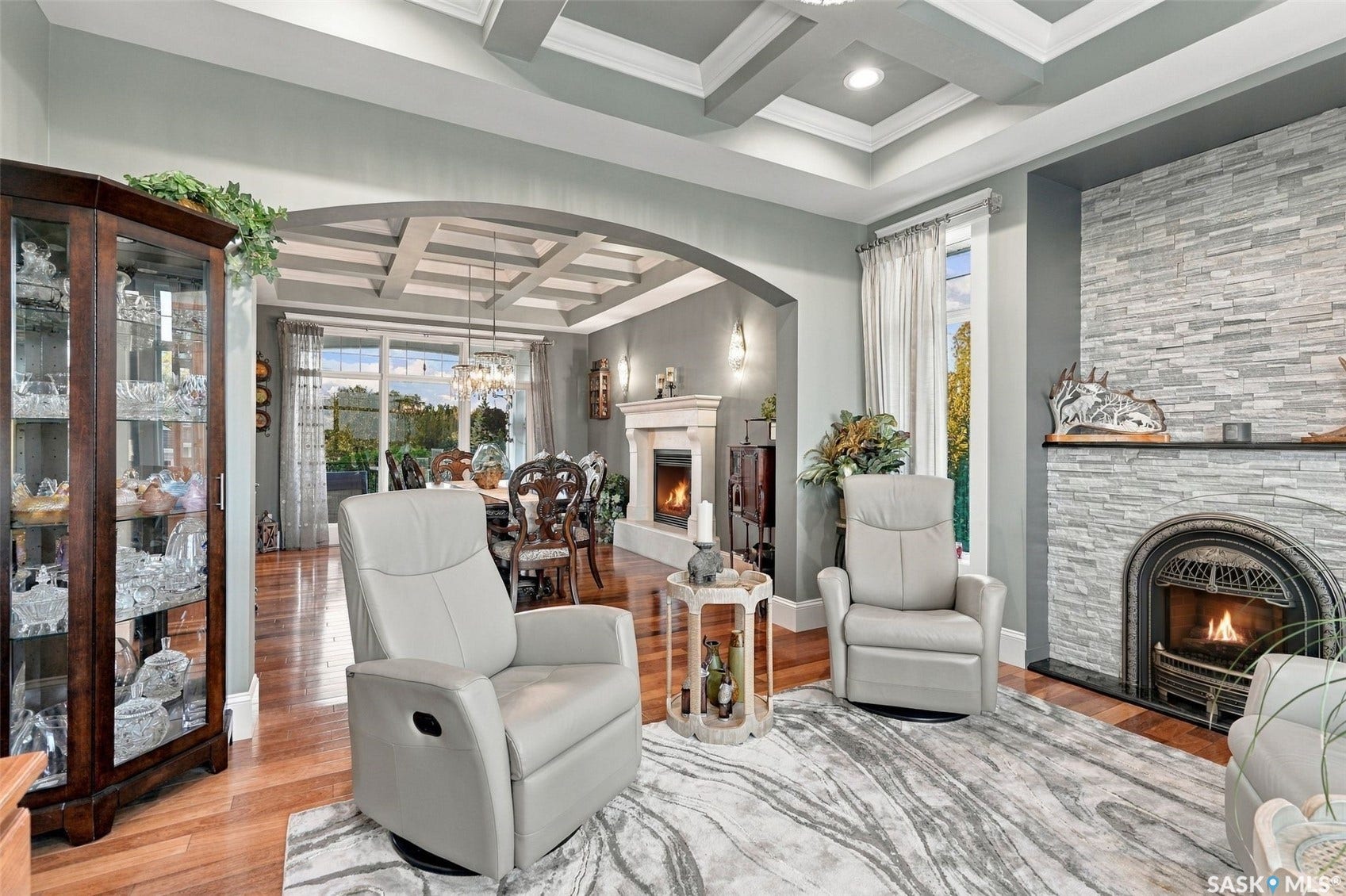 Hardwood flooring, coffered ceiling, stacked stone fireplace surround, arched doorway.