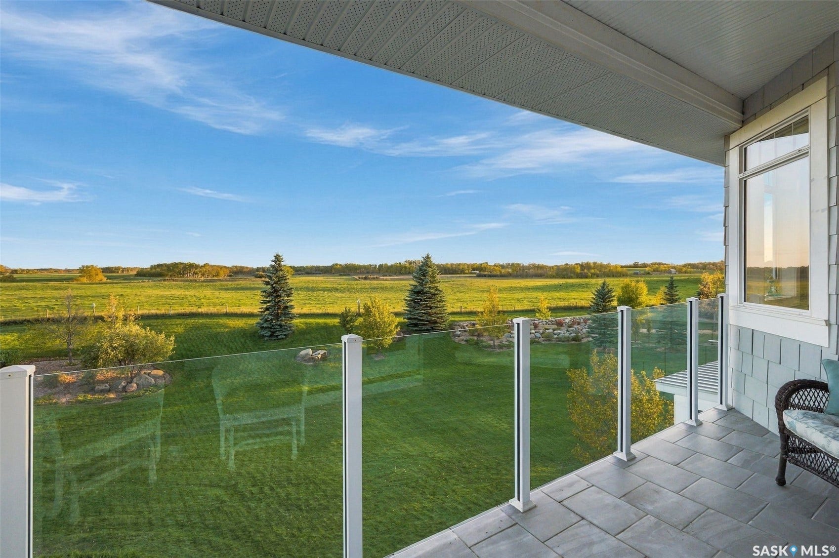 Covered balcony off primary bedroom with paver flooring, glass railing, and a window featuring horizontal siding