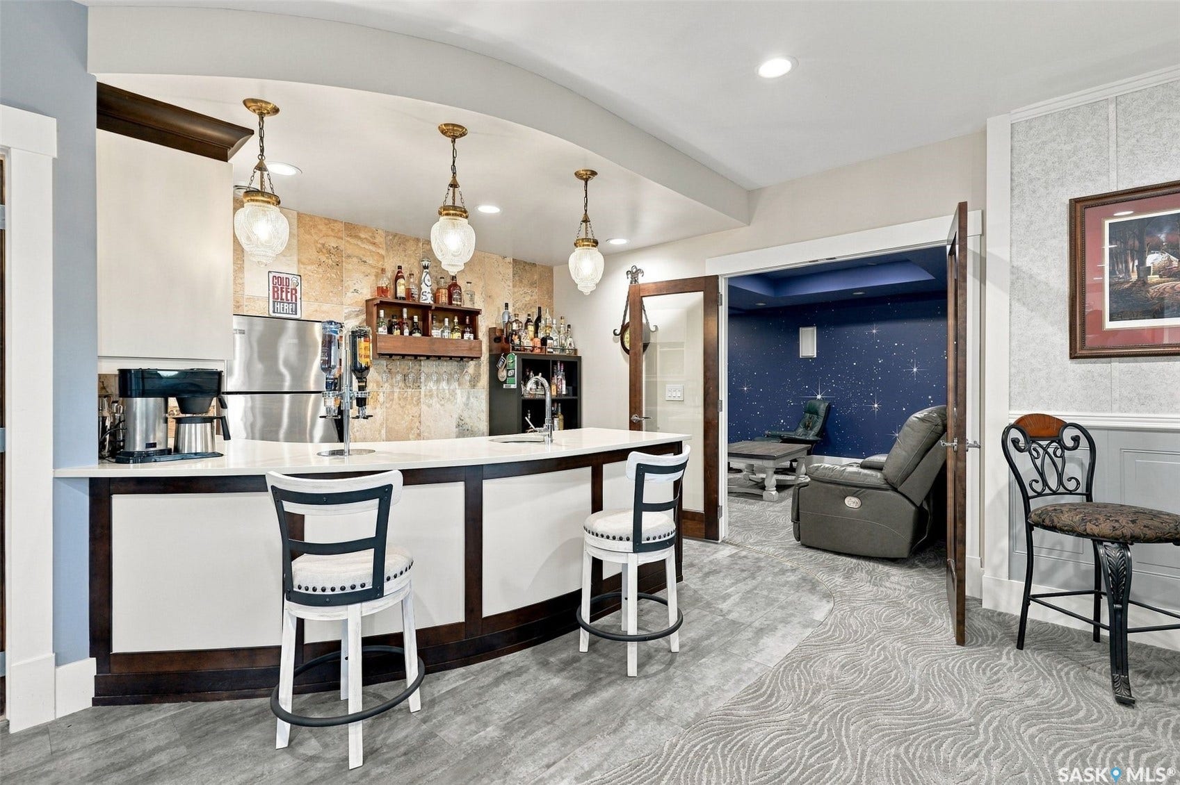 Sophisticated basement bar featuring a curved counter with black and white finishes, pendant lighting with brass accents, and a mirrored backsplash