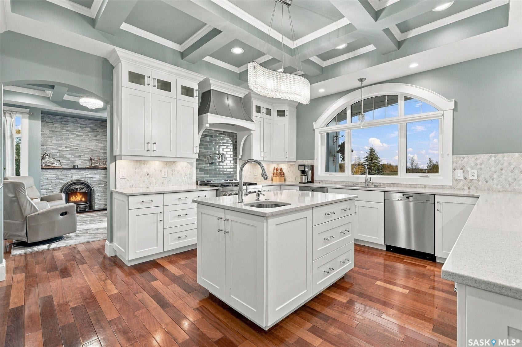 Gourmet kitchen featuring white cabinetry, center island with sink, stainless steel appliances, and an arched window overlooking the landscape