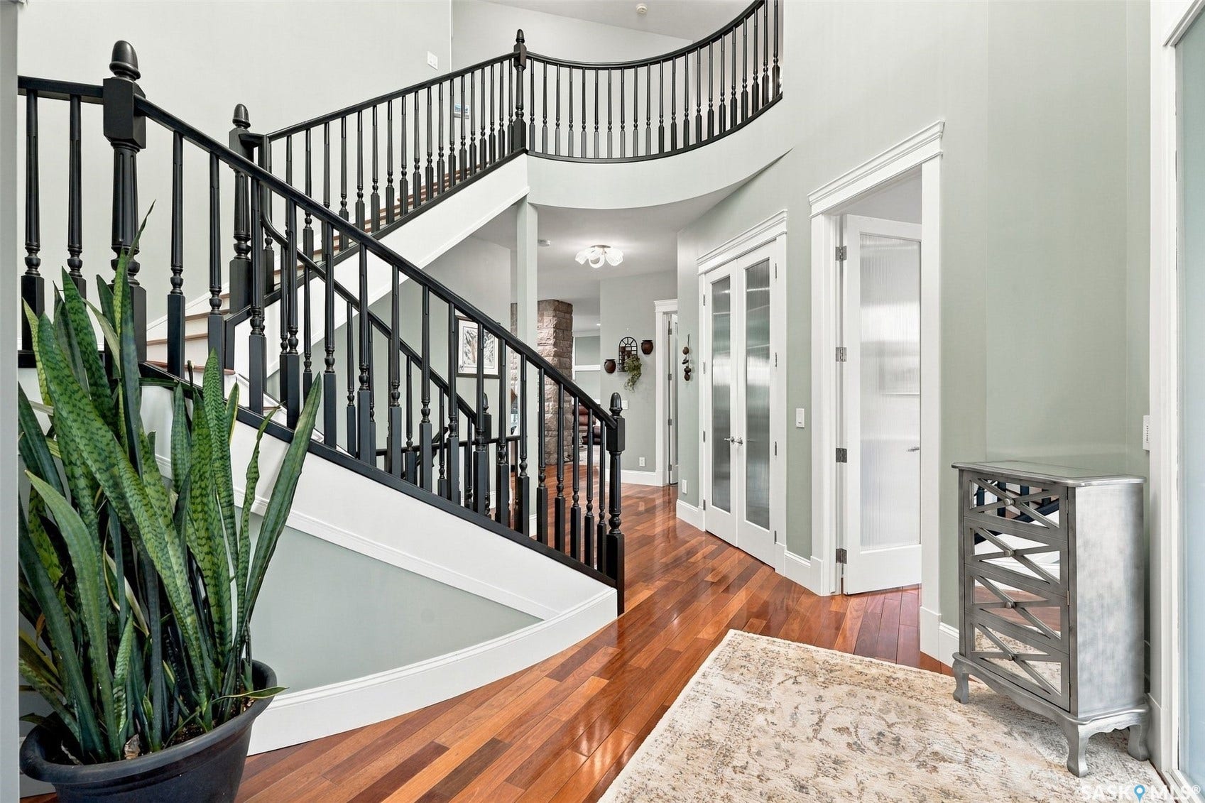 Grand staircase with black balusters, wood-finish flooring, and white trim