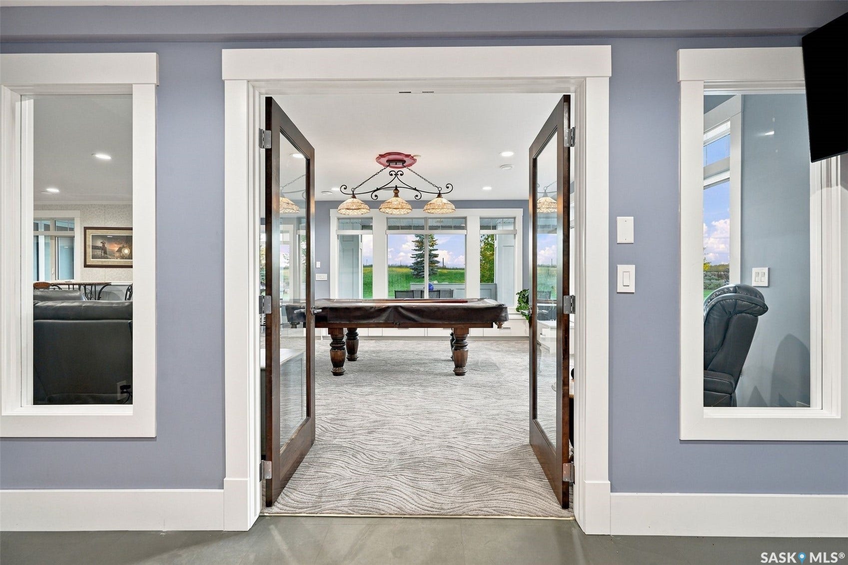 Glass-paneled French doors opening to an interior space with a pool table, featuring a decorative chandelier and multiple windows