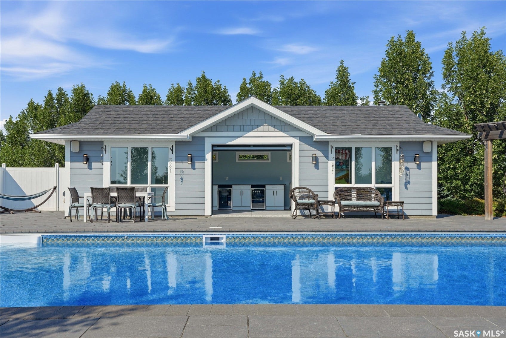 Built-in outdoor kitchen with integrated appliances, pool house with siding exterior, and a built-in outdoor bar