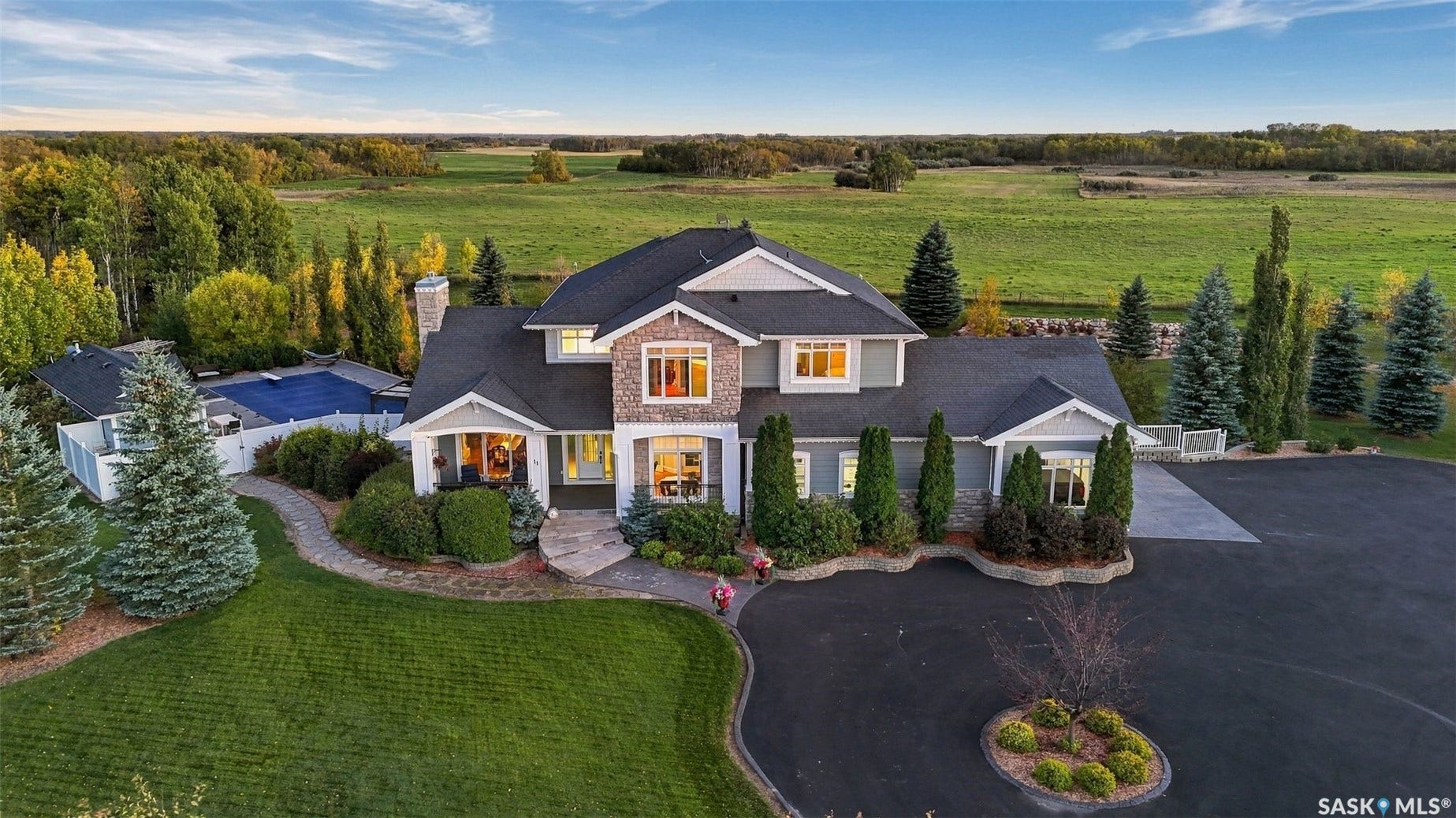 Spacious residential property featuring a stone and siding exterior, expansive paved driveway, and established landscaping