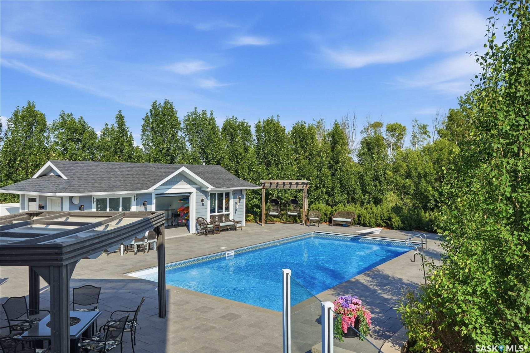 Expansive outdoor area featuring a swimming pool, a dedicated pool house with a gray shingle roof, a covered patio structure, and a surrounding paver patio