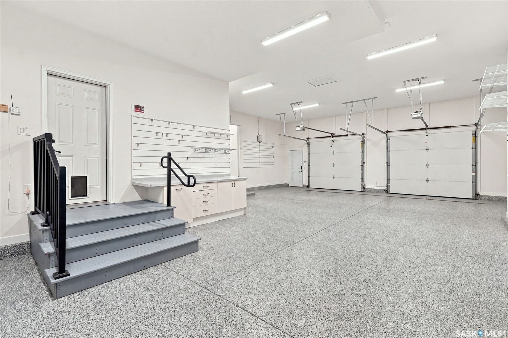 Three-car garage with an epoxy floor, built-in cabinetry, slatted wall storage, and dual garage door openers