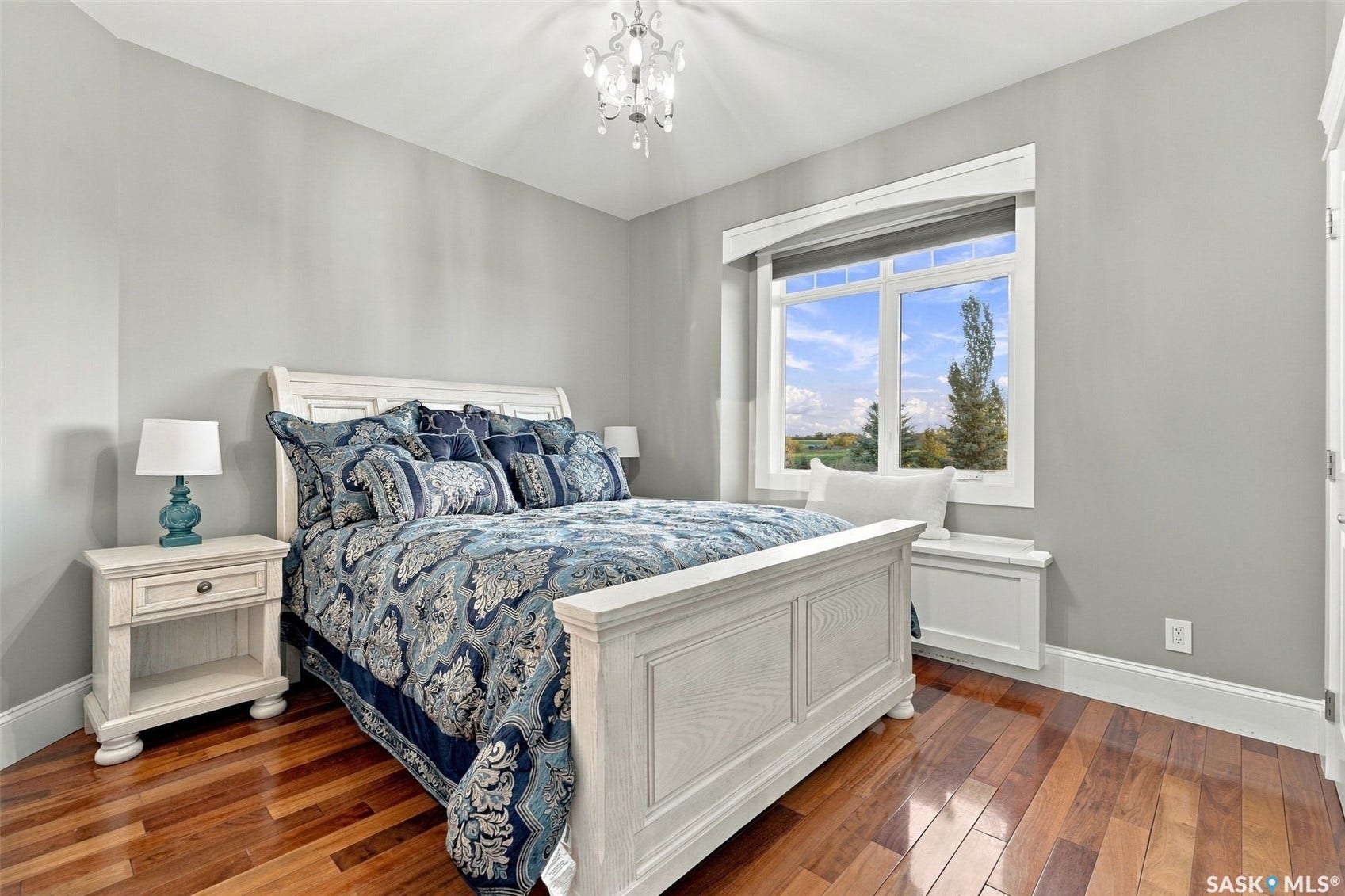 Hardwood flooring, window with bright natural light, built-in window seat, ceiling-mounted chandelier, and light gray wall finish