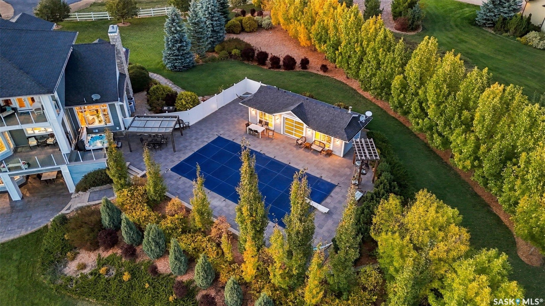 Expansive outdoor living area featuring a covered pool, a pool house with an outdoor seating area, mature privacy trees, and a multi-level deck with glass railings