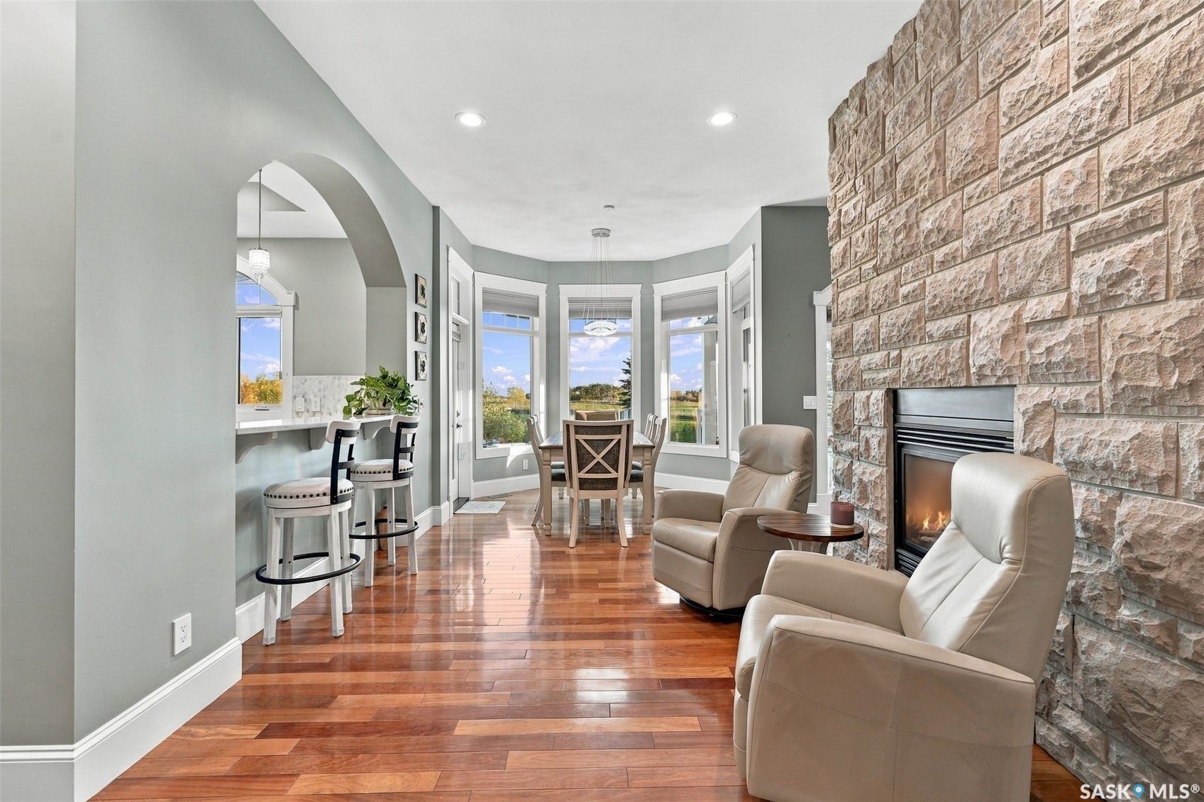 Stone-clad fireplace, wood-finish flooring, recessed lighting, arched doorway, and bay windows