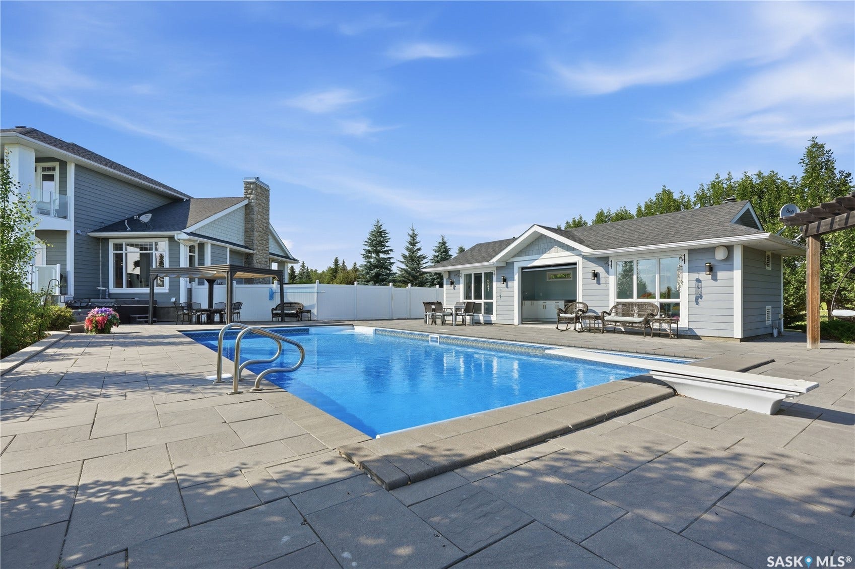 Rectangular swimming pool with integrated steps, surrounded by large format paver patio and a pool house with an overhead door
