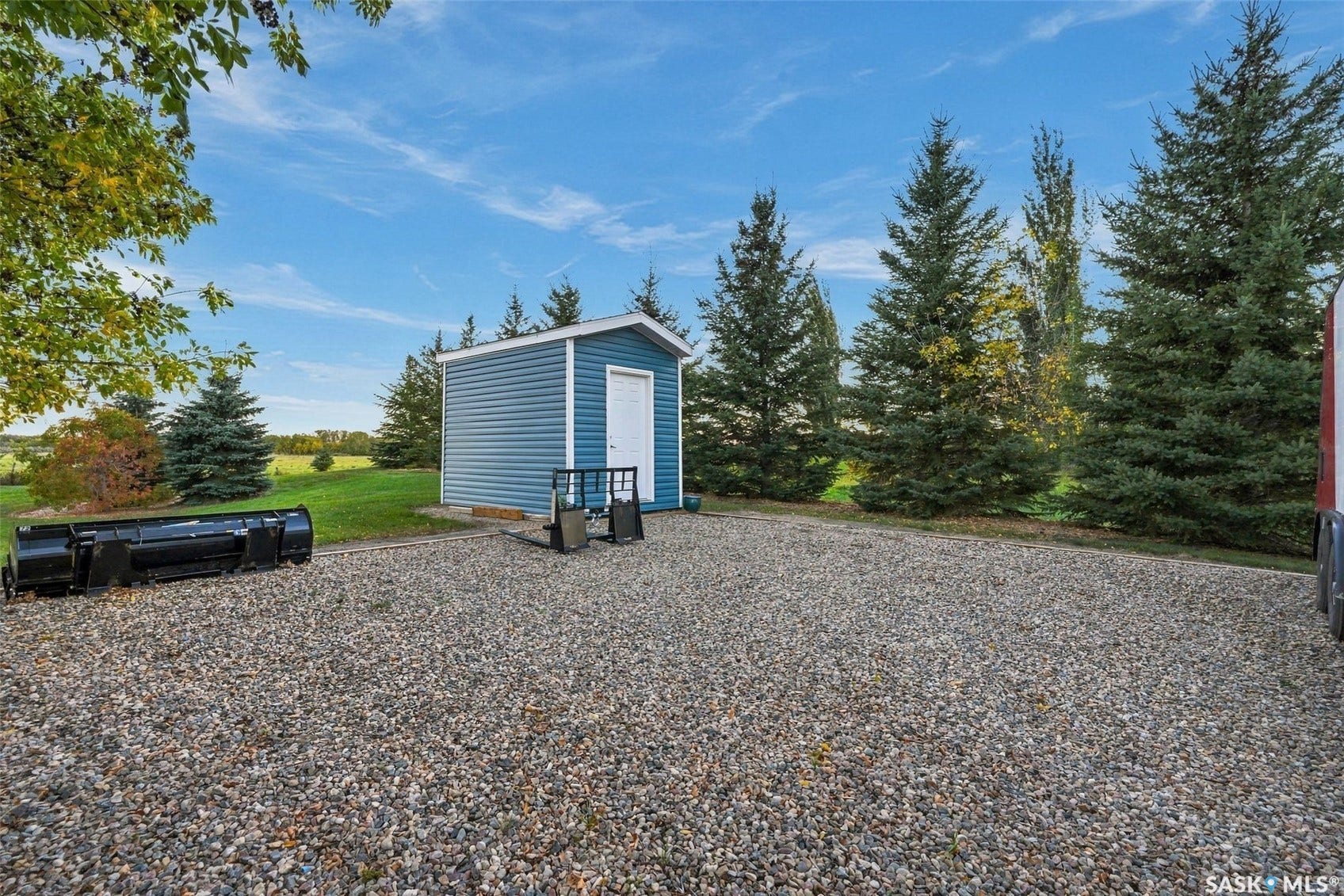 Gravel parking area featuring a storage shed with blue siding and white trim