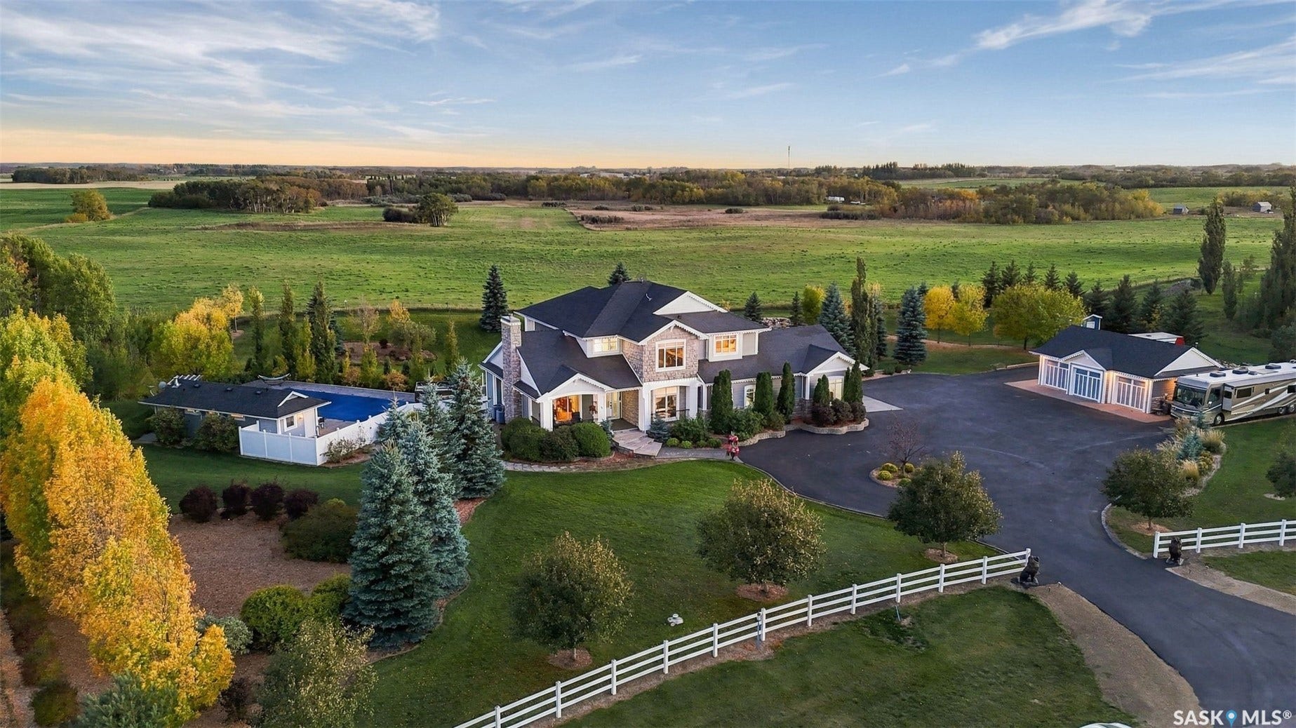 Expansive property featuring a large residence with multiple gables, a detached outbuilding, a fenced swimming pool, and a paved circular driveway
