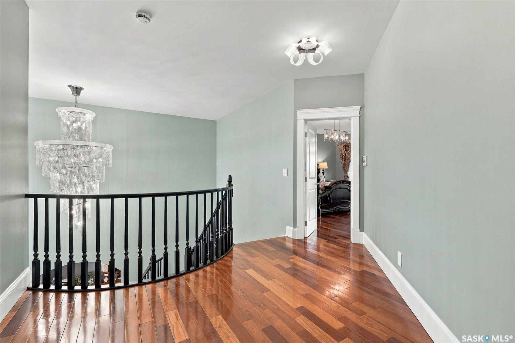 Hardwood flooring, curved black spindle railing, tiered crystal chandelier, white trim, and recessed lighting