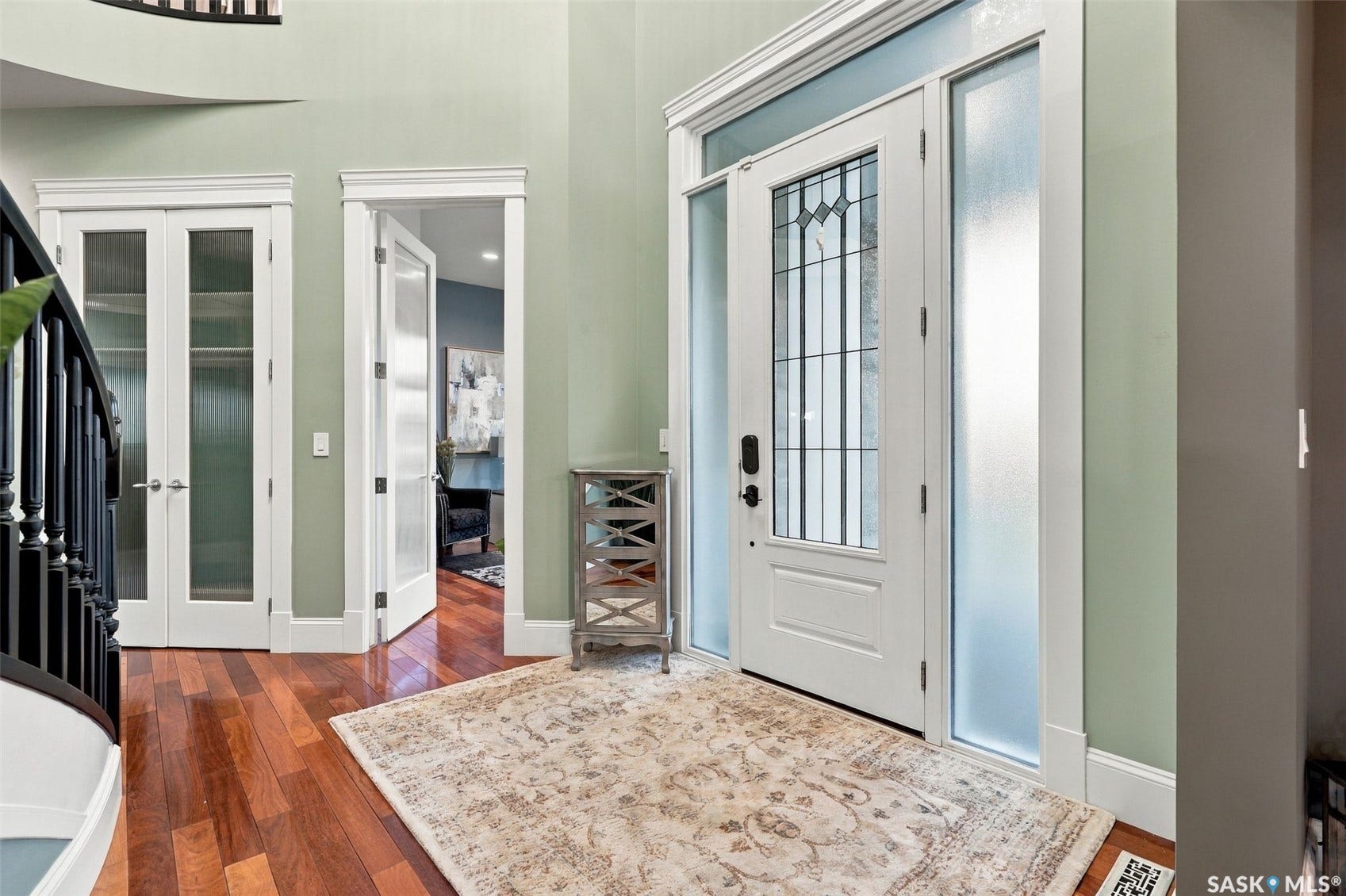 Hardwood flooring, leaded glass front door with sidelights, staircase with wood banister, and interior doors with frosted glass panels