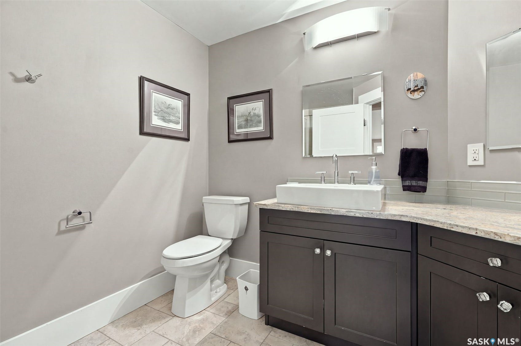 Vanity with a vessel sink, curved countertop, dark wood-finish cabinetry, and glass tile backsplash