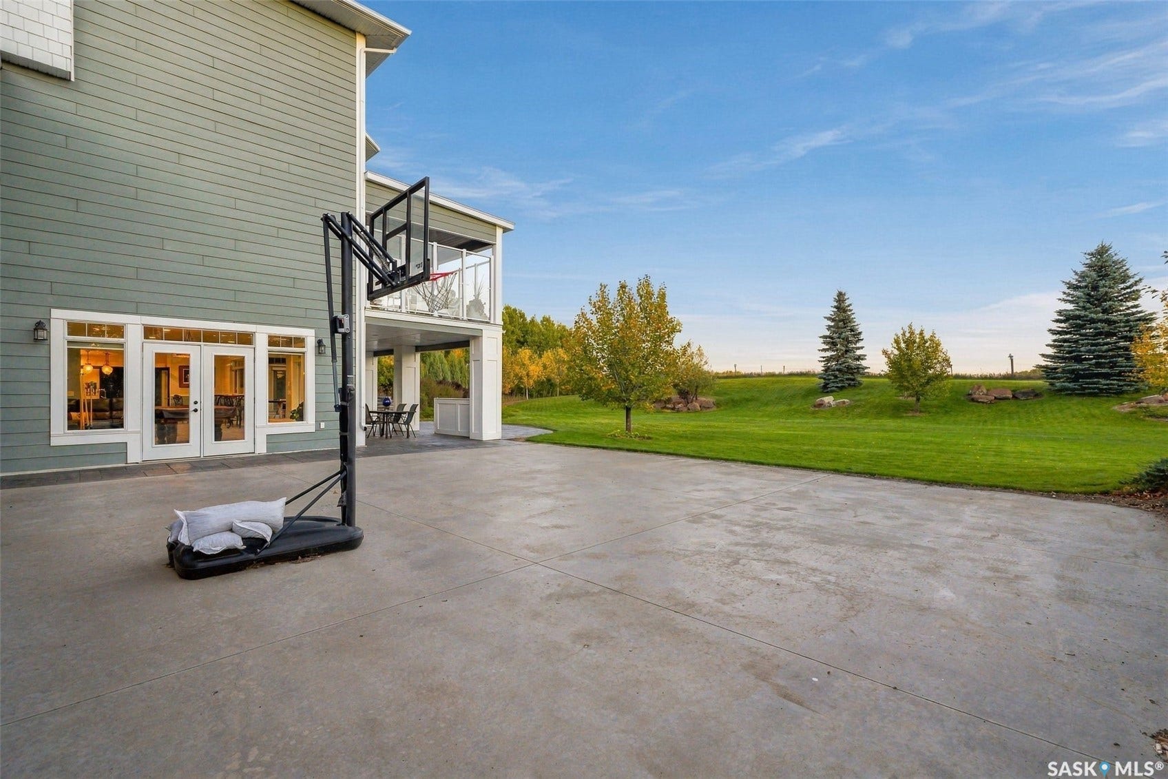 Expansive concrete patio with direct access to a manicured lawn, featuring mature trees and a covered deck