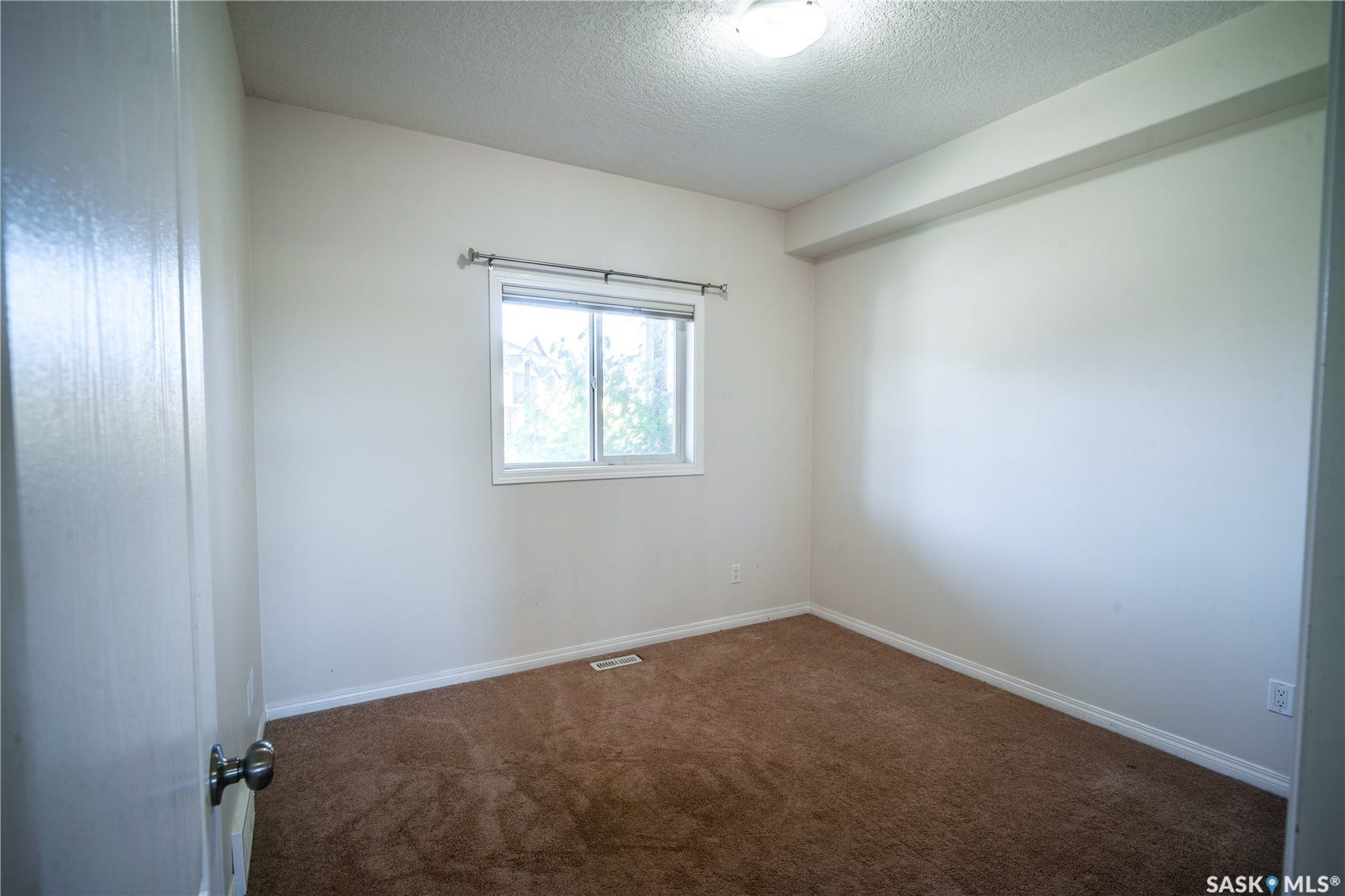 White interior walls, brown carpet flooring, and a single window with a privacy curtain rod