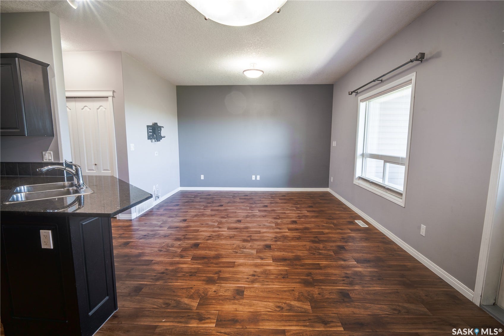Wood-finish flooring, dark cabinetry with stainless steel sink, large window with blinds, and recessed lighting