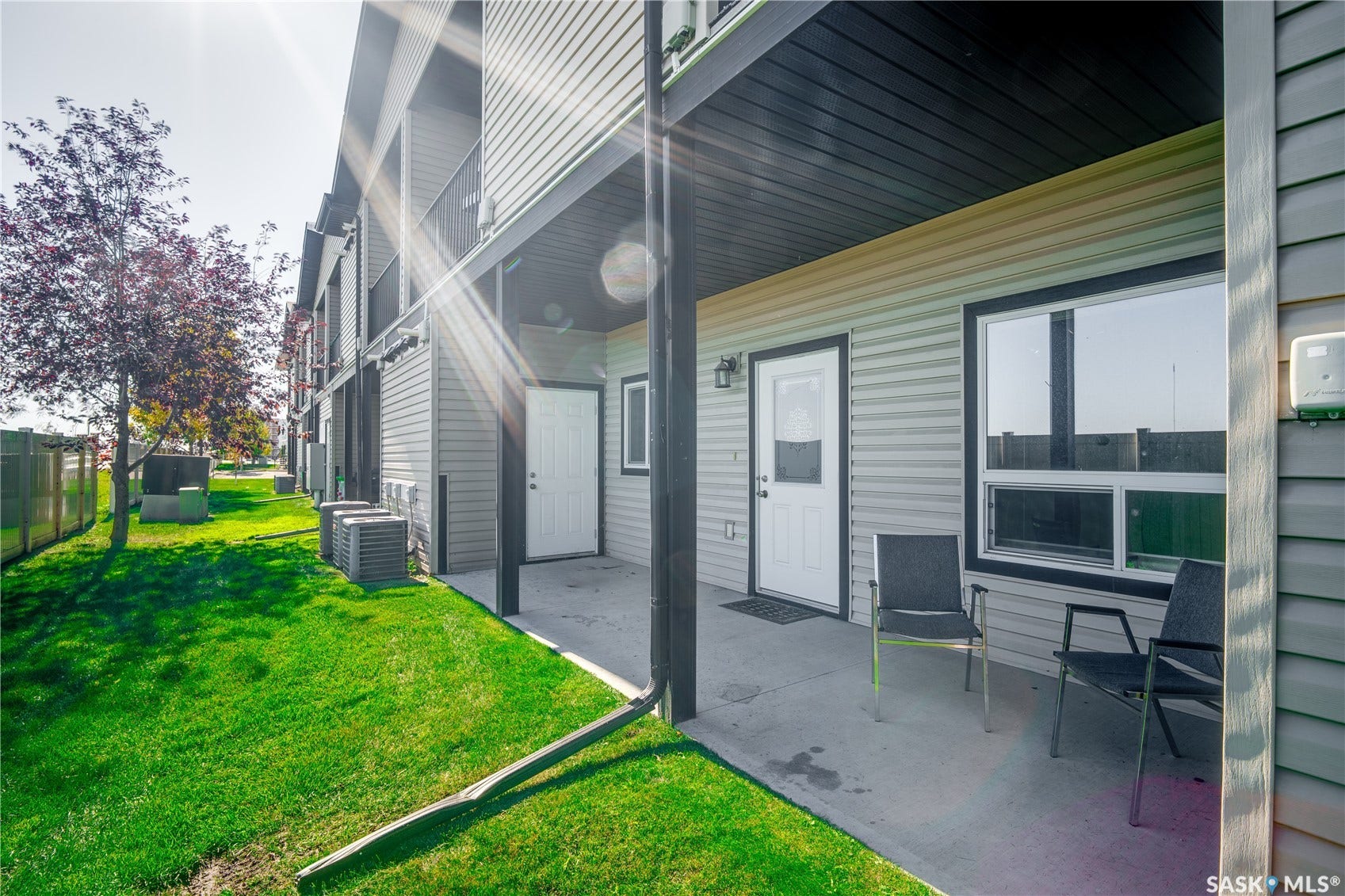 Ground-level patio with concrete slab, white exterior door, and large window with black trim