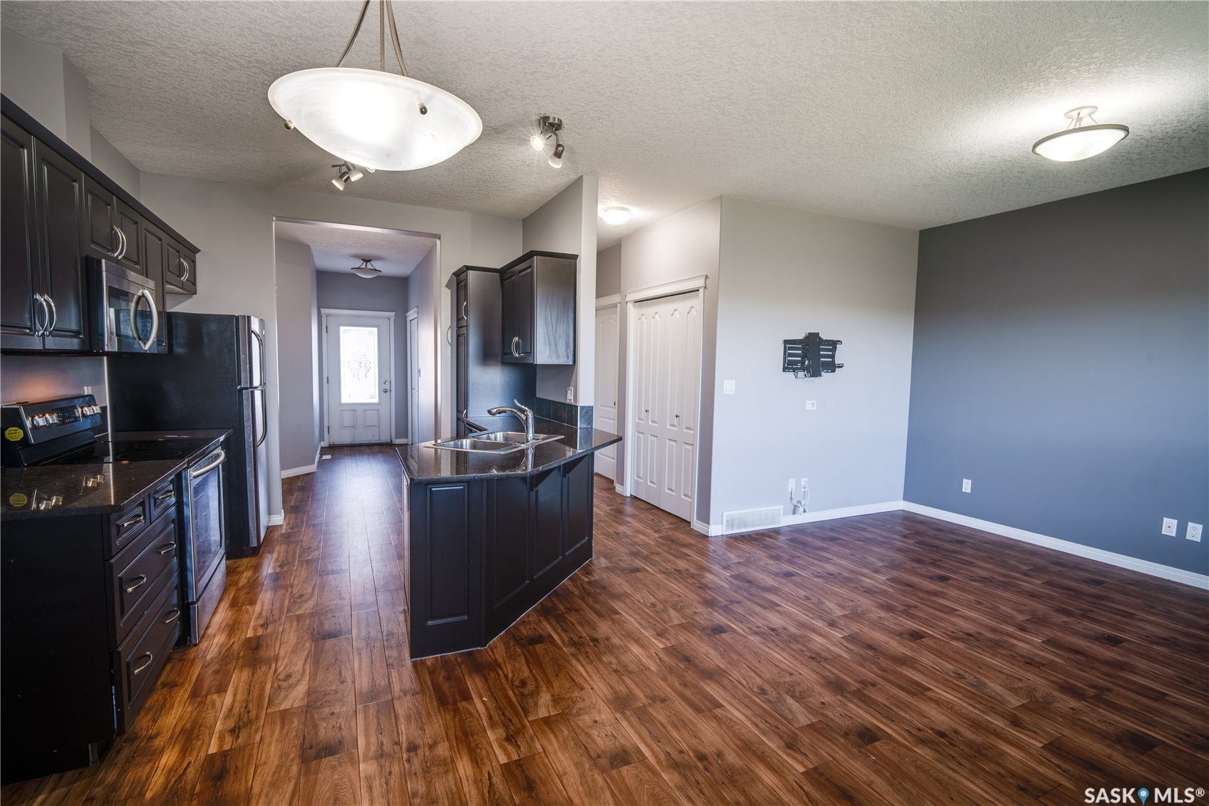 Kitchen featuring dark wood-finish cabinetry, built-in stainless steel appliances, and a central island with an undermount sink