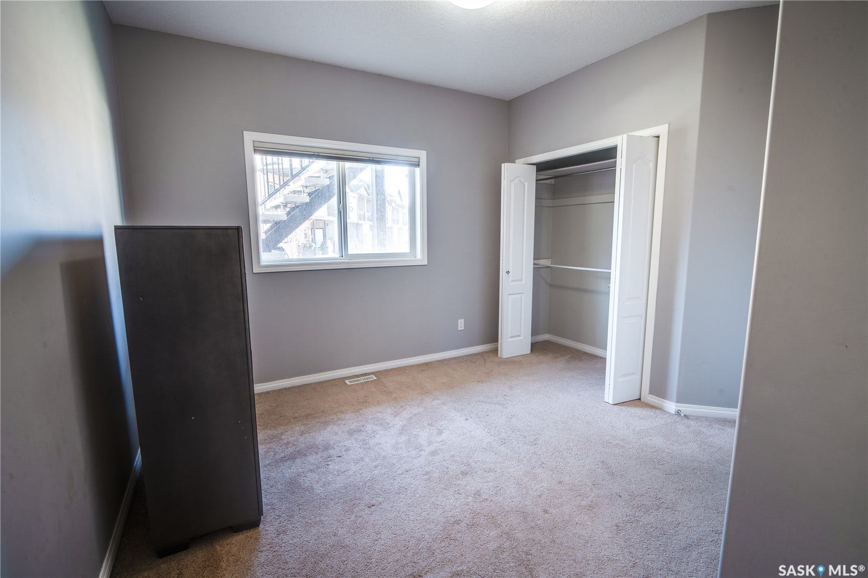 Spacious bedroom with neutral taupe walls, wood-finish flooring, and abundant natural light from a large window