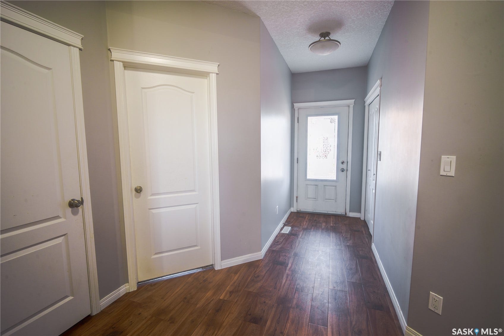 Hallway featuring wood-finish flooring, white paneled doors, and a decorative frosted glass entry door