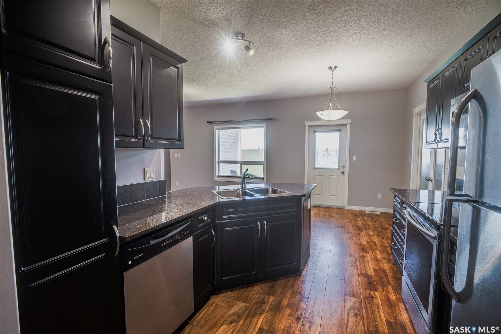 Kitchen with dark wood-finish cabinetry, stainless steel dishwasher, and dark countertops