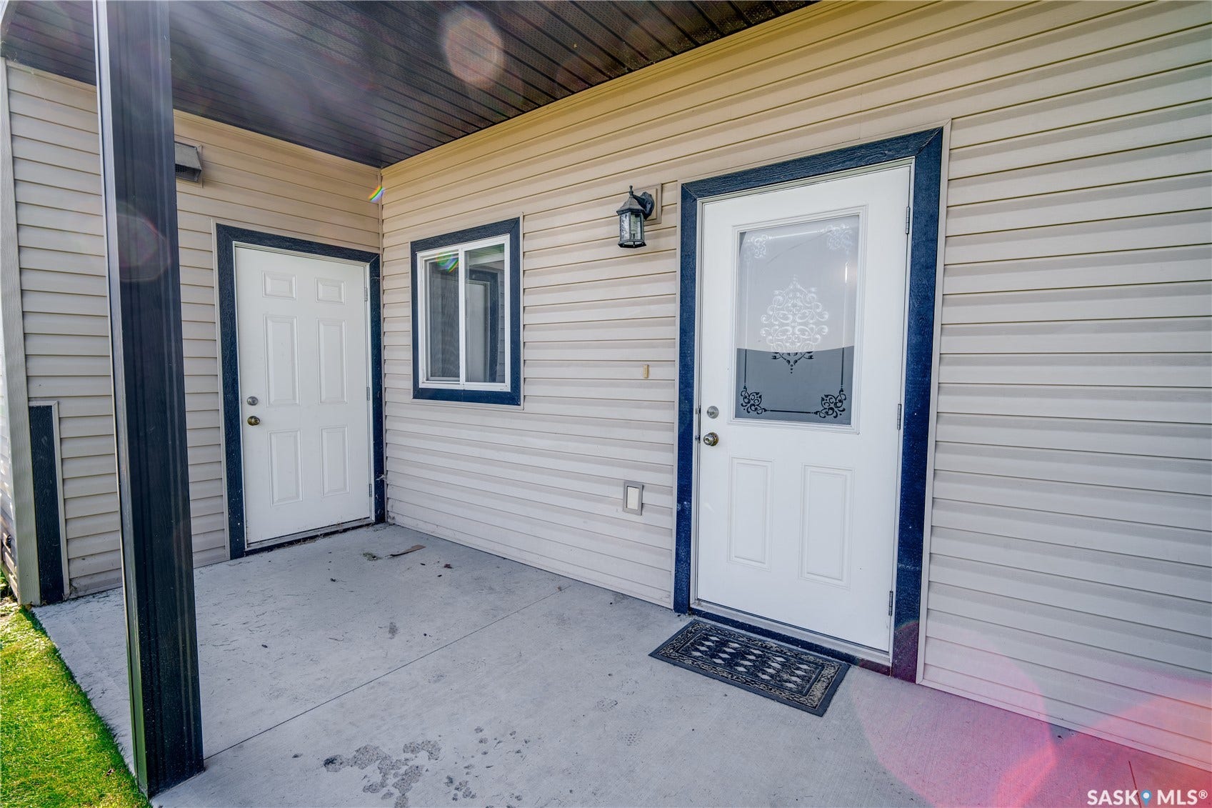 Exterior entry featuring a white panel door with decorative glass, beige siding, a concrete landing, and a black exterior light fixture