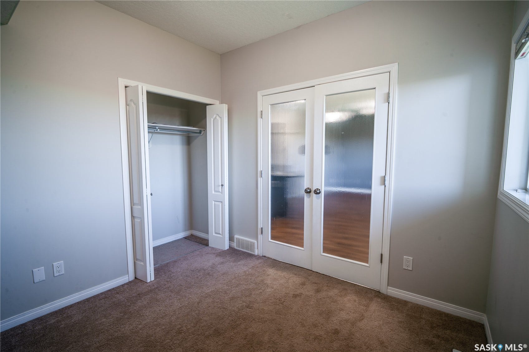 Carpeted room with light neutral walls, white trim, a double-door closet with bifold doors, and French doors featuring frosted glass panels
